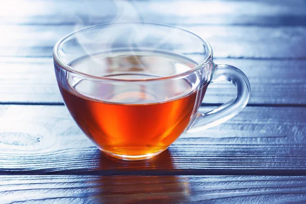 Mavi ışıklı soğuk arka planda, ahşap masanın üzerinde bir fincan kahverengi sıcak çay.