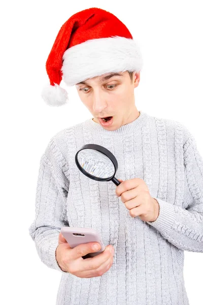 Překvapený Mladý Muž Santa Klobouku Lupou Při Pohledu Mobilní Telefon — Stock fotografie