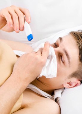 Evdeki yatakta termometresi ve mendili olan genç adam.