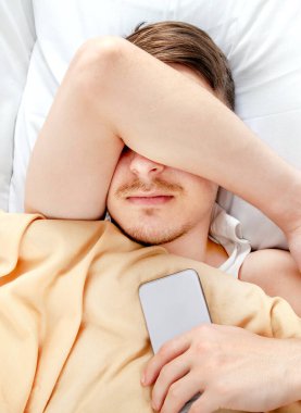 Genç adam cep telefonuyla yatağında uyuyor.