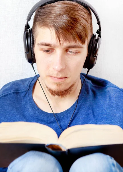 Kulaklıklı Genç Adam Evdeki Duvarda Bir Kitap Okuyor — Stok fotoğraf