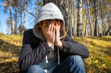 Üzgün genç adam, yüzünü kapat ve sonbahar ormanında yalnız otur.