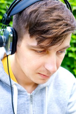 Yeşil yapraklı kulaklıklı genç adam dışarıda.