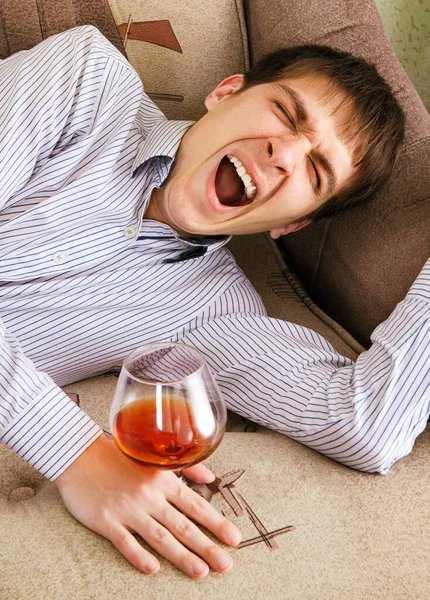 ブランデーのグラスを持つ疲れた若い男は家でソファの上で疲れている — ストック写真