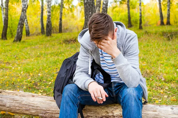 Trauriger Junger Mann Mit Zigarette Sitzt Herbstwald Auf Dem Baumstamm — Stockfoto