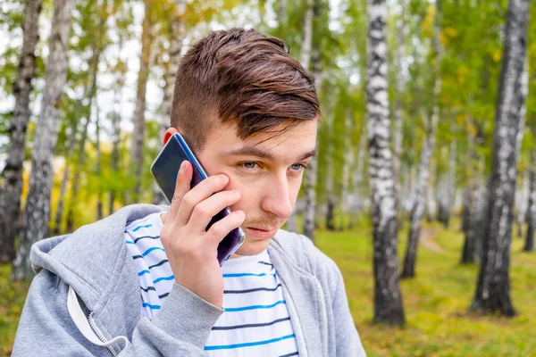 Szomorú Fiatalember Mobiltelefonnal Őszi Erdőben — Stock Fotó