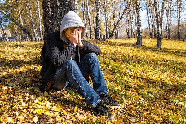 Üzgün genç adam, yüzünü kapat ve sonbahar ormanında yalnız otur.