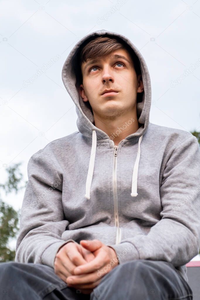 Sad Young Man in a Hoodie on the Sky Background outdoor