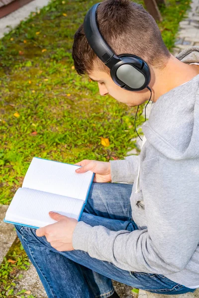 Unge Man Hörlurar Läser Bok Utomhus — Stockfoto