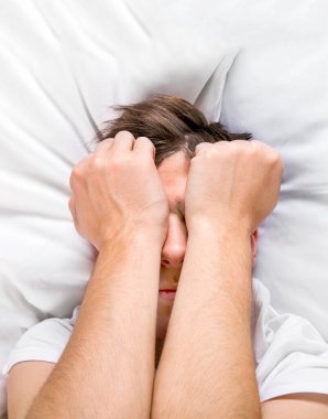 Yataktaki üzgün genç adam yüzünü kapat.