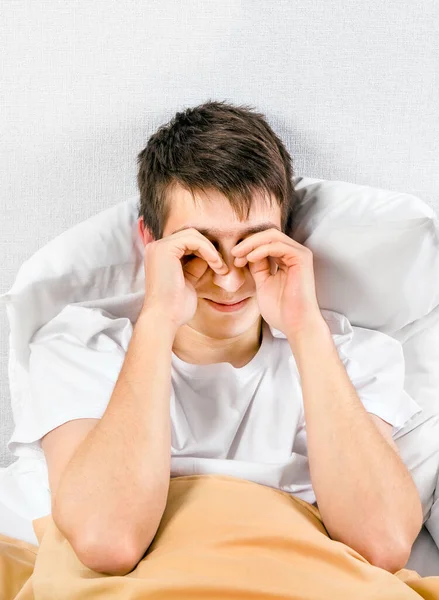 眠い若い男は壁によってベッドで彼の目をこすり — ストック写真