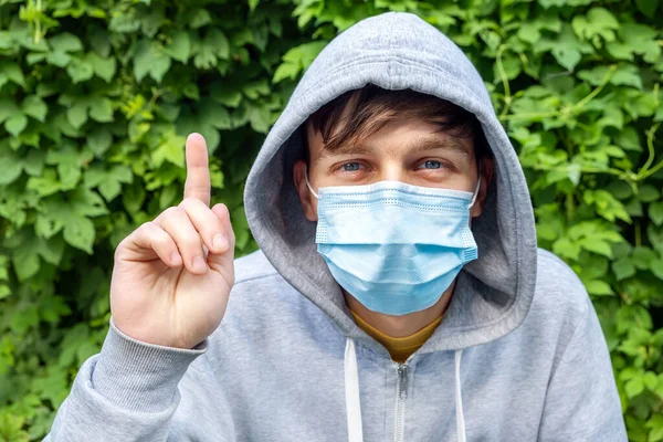 Grip Maskeli Genç Adam Yeşil Yapraklar Arkaplanında Parmak Hareketi Yapıyor — Stok fotoğraf