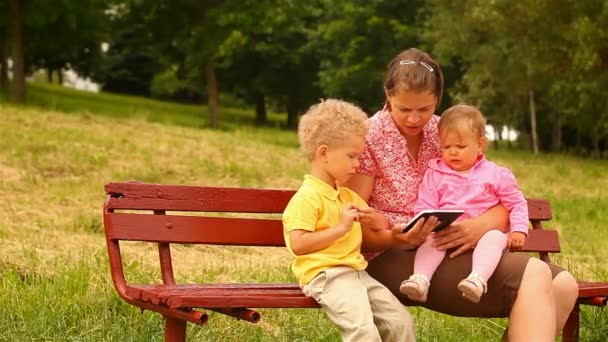 Мать и двое детей, чтение и просмотр планшетных компьютеров — стоковое видео