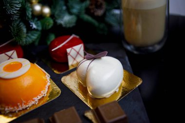 Tatlılar (çeşitli şekillerde ve renklerde mus kekleri) ve çikolata parçaları. Arka planda Noel için süslenmiş ladin dalları görülüyor