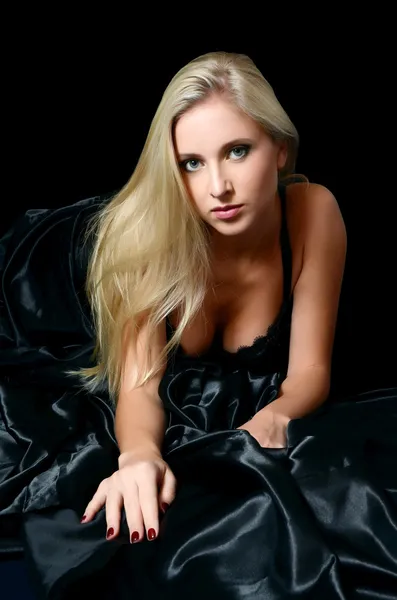 Das schöne Mädchen die Blondine auf einem schwarzen Bett — Stockfoto
