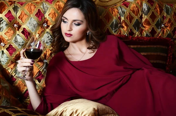 Donna sensuale con un bicchiere di vino rosso su un magnifico divano — Foto Stock