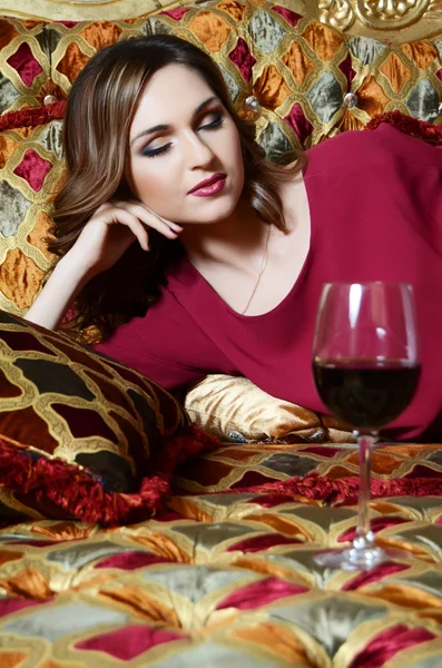 Érzéki nő, egy pohár vörösbor egy csodálatos kanapé — Stock Fotó