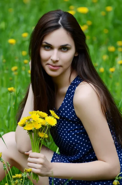 De mooie vrouw in het veld met paardebloemen — Stockfoto