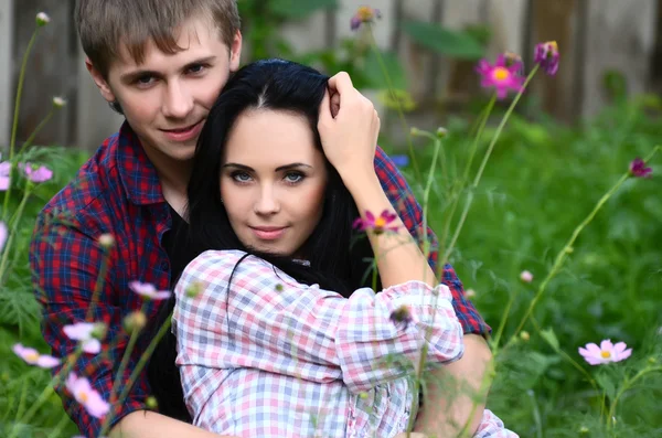 Pareja joven esmaltada en el campo con flores — Foto de Stock