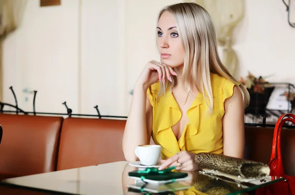 A bela mulher em um vestido amarelo atrás de uma mesa no café — Fotografia de Stock