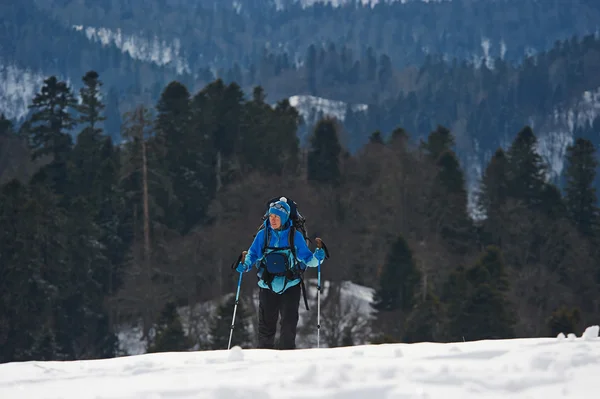 Kvinnlig backpacker klättrar en kulle i bergen på vintern — Stockfoto