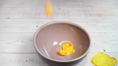 Patates cipsleri beyaz ahşap masada duran kahverengi seramik kaseye düşüyor..