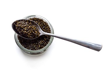 Cam kavanoz ve beyaz üzerine izole edilmiş bir kaşık siyah havyar. Doğal mersin balığı lüks lezzeti yakın plan. Deniz ürünleri mezesi..