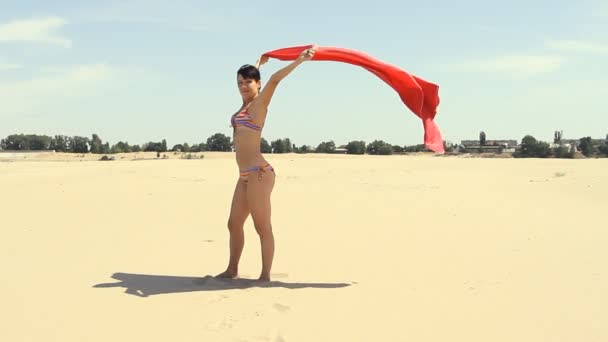 Jonge vrouw met rode sarong wind-geblazen permanent op het strand — Stockvideo