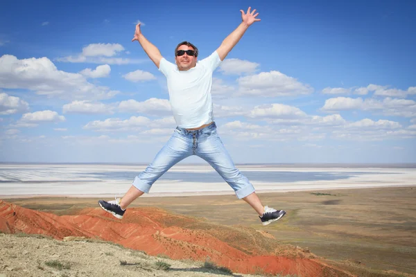 Young man in sunglasses jumping over blue sky — Stock Photo, Image