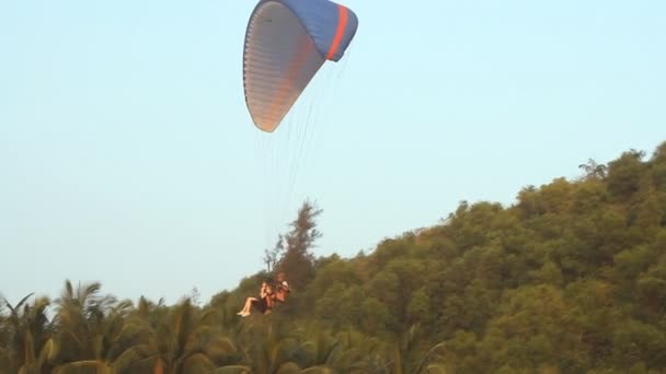 Parapente sobre las montañas está aterrizando en los trópicos contra el cielo azul claro — Vídeos de Stock