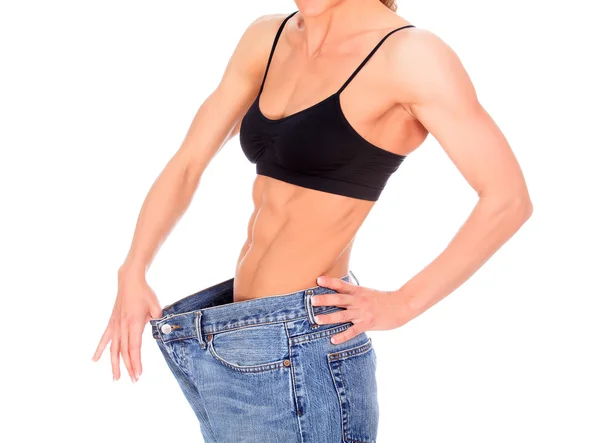 Kvinna med stark abs visar sin gamla stora jeans — Stockfoto