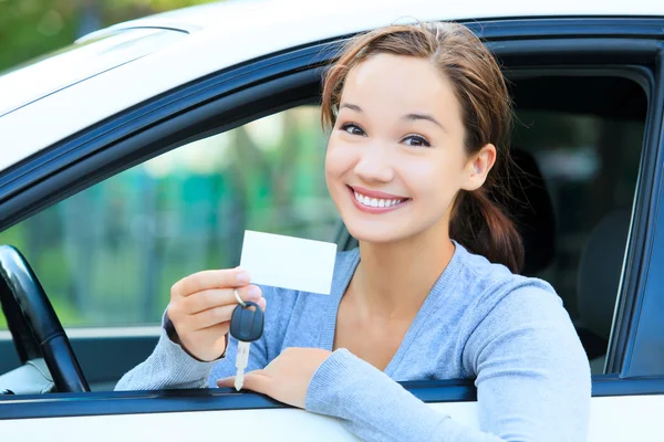 Chica en un coche mostrando una llave y una tarjeta blanca vacía — Foto de Stock