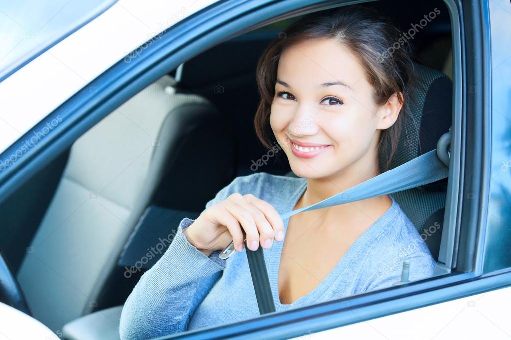 Smiling young woman in car fastens seat belt