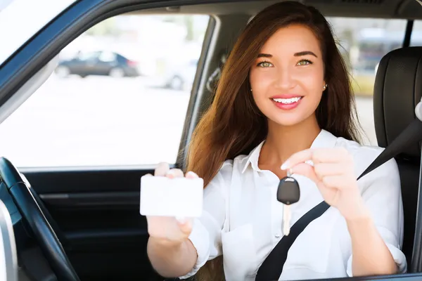 Девушка в машине с ключом и пустой белой карточкой — стоковое фото