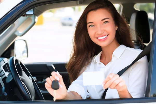 Chica en un coche mostrando una llave y una tarjeta blanca vacía — Foto de Stock