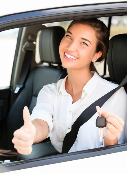 Счастливая девушка в машине показывает ключ и большой палец вверх жест — стоковое фото