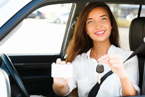 Mädchen im Auto zeigt einen Schlüssel und eine leere weiße Karte — Stockfoto