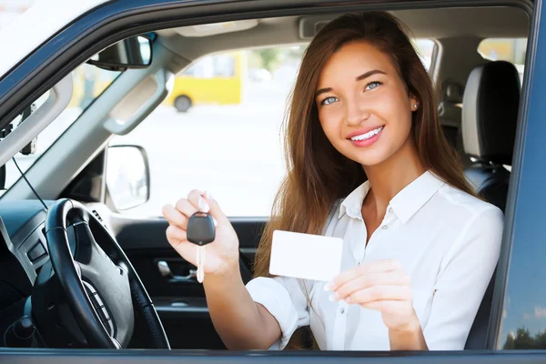 Chica en un coche mostrando una llave y una tarjeta blanca vacía — Foto de Stock