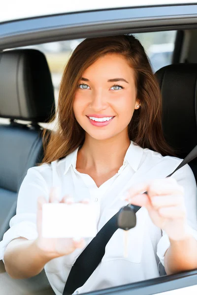 Chica en un coche mostrando una llave y una tarjeta blanca vacía — Foto de Stock