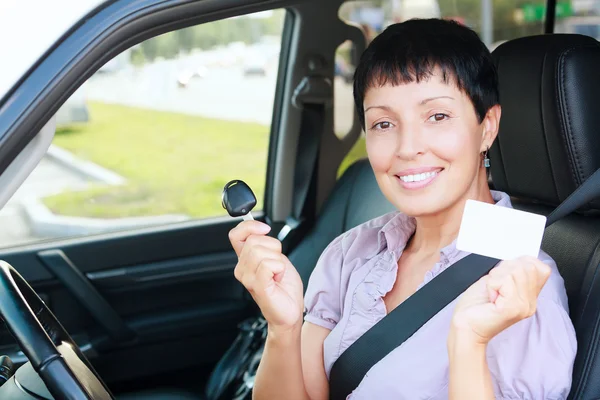 Mulher sorridente sênior segurando chave do carro e cartão branco vazio — Fotografia de Stock