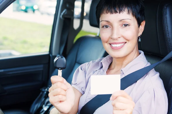 Mujer sonriente senior sosteniendo la llave del coche y la tarjeta blanca vacía —  Fotos de Stock