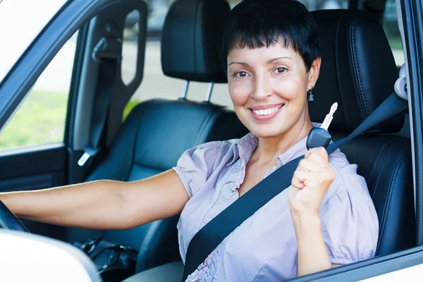 Senior mulher segurando chave do carro e sorrindo para você de um carro — Fotografia de Stock