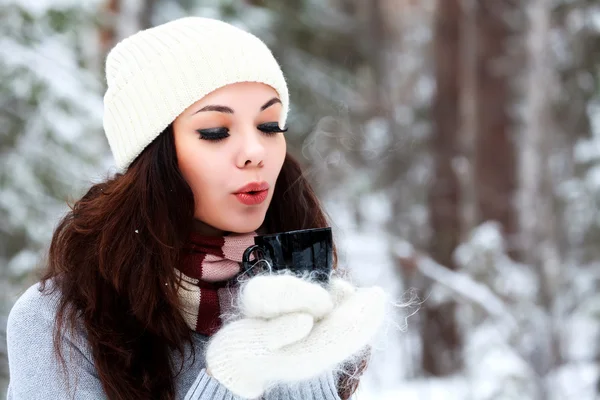 Vacker ung kvinna i Stickad mössa och tröja blåser på varm te — Stockfoto