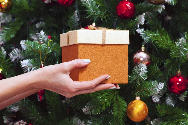 Γυναικεία Χέρια Κρατώντας Ένα Κουτί Δώρου Κατά Διακοσμημένα Χριστουγεννιάτικο Δέντρο — Φωτογραφία Αρχείου