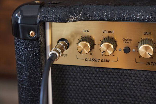 Cable plugged in to a guitar amplifier, adjusting gain and volume, controls detail