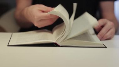 Bir odada bir masada kitap, bir adam okuyor, bir göz atıyor.