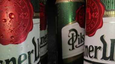 BUDAPEST, HUNGARY - CIRCA 2020: Cans of Pilsner Urquell, popular Czech beer brewed in Plzen, camera with probe lense moving in between them, waterdrops, hand taking one can