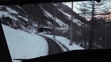 İsviçre Alplerinde Zermatt hattında tren yolculuğu, sürücülerin perspektifi karlı kış akşamlarında, dağların arasında raylar.