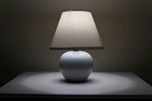Small lamp glowing in bedroom night stand by the bedside, close up, dim room
