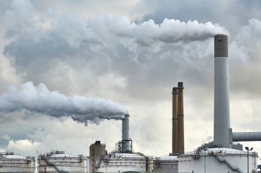 Ön planda petrol ambarları olan tütsülenmiş santral bacaları.
